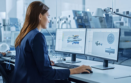 Yüksek teknolojili mühendislik ve tasarım çalışmaları yapan kadın mühendis, iki ekran kullanarak ürün modelleme ve CAD tasarımları yapıyor, yenilikçi çözümler üzerinde çalışıyor.