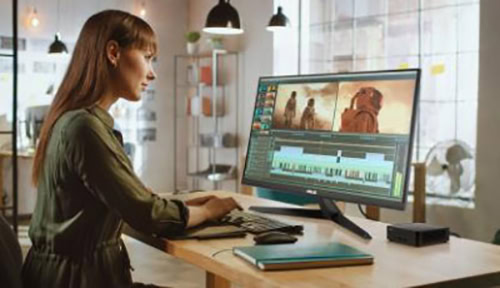 Görüntü düzenleme yazılımı ile çalışan kadın, laptop ve masaüstü bilgisayar ekranında video düzenleme yapıyor. Modern ofis ortamında teknolojik ekipmanlar ve profesyonel çalışma alanı.